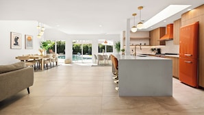 A modern kitchen with a central island, a dining area with a pool view, and a living room with a sofa.