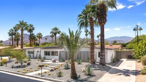 A modern house with a driveway, palm trees, and a mountain backdrop.