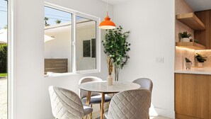 A dining area with a round table, four chairs, a vase with plants, and a hanging orange pendant light.