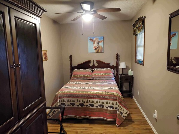 Une chambre à coucher avec un lit en bois, un ventilateur de plafond, une fenêtre avec des stores et un tableau accroché au mur.