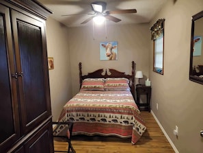 Un dormitorio con una cama de madera, un ventilador de techo, una ventana con persianas y un cuadro colgado en la pared.