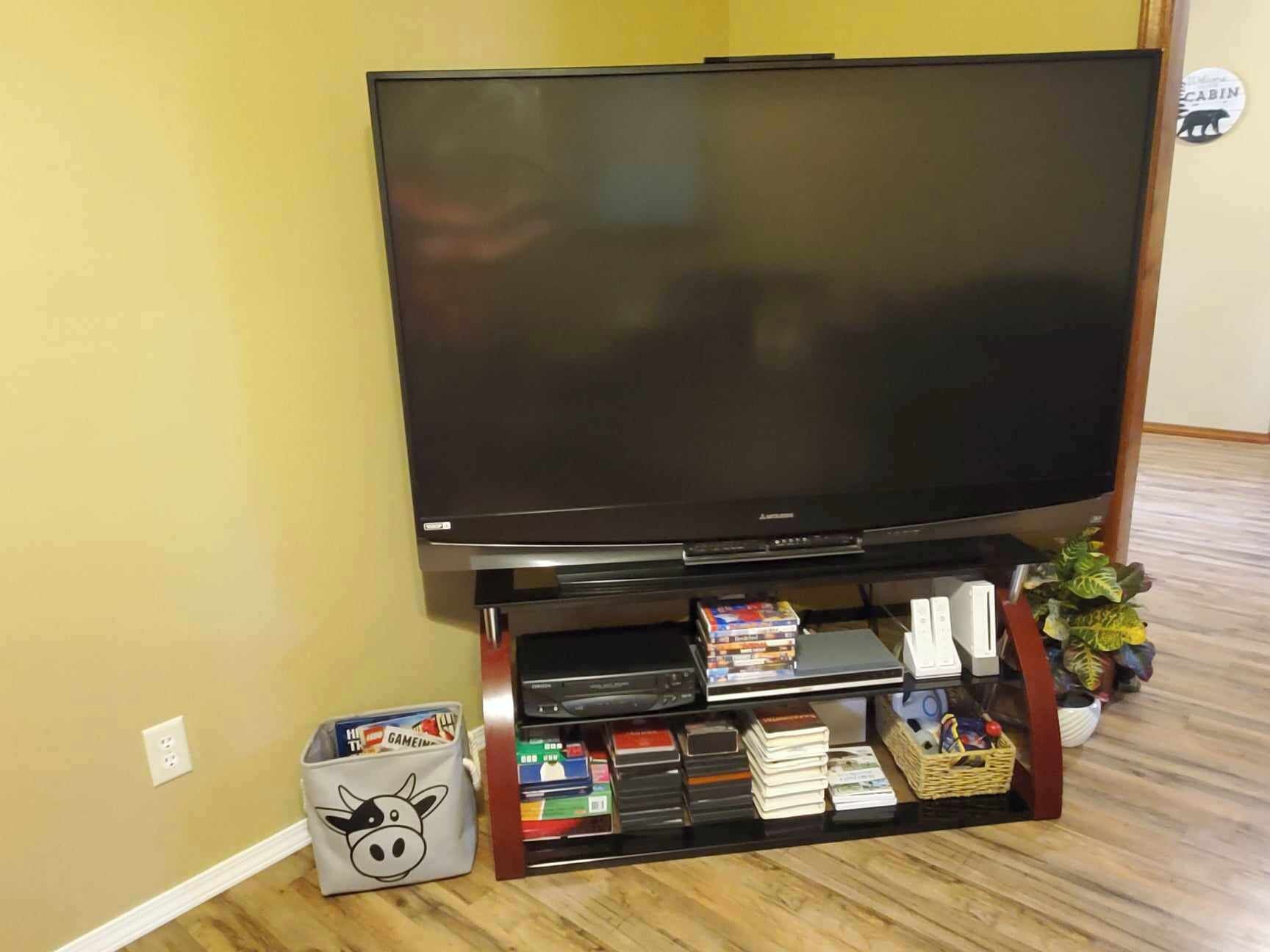 Ein Flachbildfernseher auf einem Holzständer mit Ablage darunter für Bücher und DVDs.