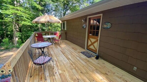 Eine Holzterrasse mit Tisch, Stühlen, einer Tür und einem kleinen Teppich.