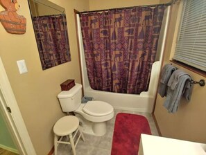 Ein Badezimmer mit Toilette, Waschbecken, einer roten Badmatte, einer Duschvorhang mit Tiermotiven und einem Handtuchhalter mit Handtüchern.