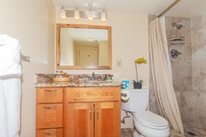 Un baño con tocador de madera, lavabo, espejo, inodoro y zona de ducha.