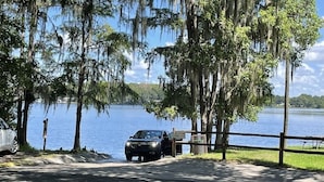 A parking area with a car and a sign, surrounded by trees and a body of water.