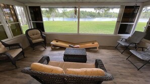 A sunroom with wicker furniture, a wooden bench, and a view of a lake.