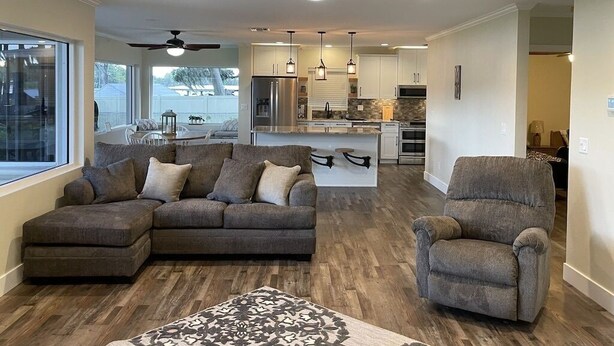 A spacious living room with a large sectional sofa, a smaller armchair, and a patterned rug. A ceiling fan and recessed lighting are visible.