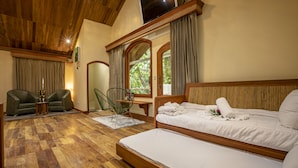 Ein Zimmer mit Holzbalkendecke, einem Bett mit weißer Bettwäsche, einer Couch, einem Sessel und einem Fernseher an der Wand.
