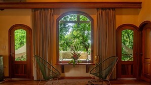 Ein Zimmer mit einem großen Bogenfenster, zwei Stühlen, einem kleinen Tisch und einer Holztür.
