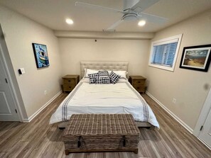 A bedroom with a large bed, two bedside tables, a ceiling fan, and a window with blinds. - Beautiful Renovated Condo 2nd Ocean Block (Rehoboth Beach)