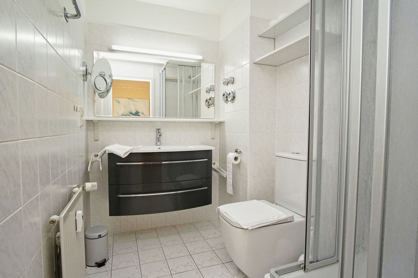 A modern bathroom with a white sink, dark vanity, toilet, and a glass shower enclosure.