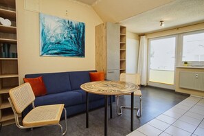 A modern living room with a blue sofa, two wicker chairs, a round table, and a large abstract painting on the wall. - Appartementanlage Eldena Wohnung Nr. 10 - Appartements Eldena (Middelhagen)