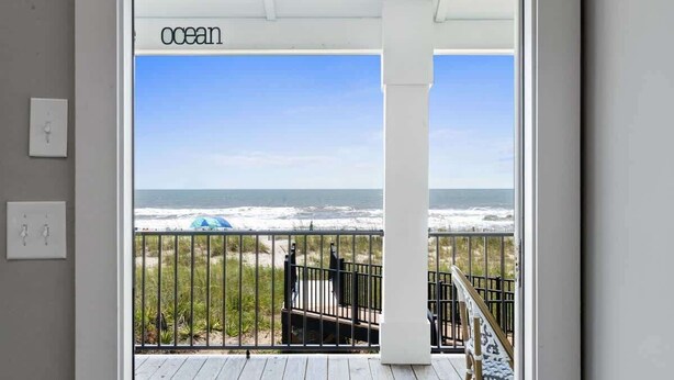 A balcony with a view of the ocean, a white column, and a railing. - Cake by the Ocean by Brunswick Vacation Rentals: Fully Renovated Oceanfront Home (Holden Beach)