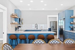 A modern kitchen with blue cabinetry, a central island, and bar stools. - Cake by the Ocean by Brunswick Vacation Rentals: Fully Renovated Oceanfront Home (Holden Beach)