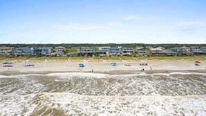 A beachfront hotel with multiple buildings, a sandy beach, and waves. - Cake by the Ocean by Brunswick Vacation Rentals: Fully Renovated Oceanfront Home (Holden Beach)