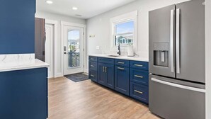 A modern kitchen with a stainless steel refrigerator, dark blue cabinets, and a white countertop. - Cake by the Ocean by Brunswick Vacation Rentals: Fully Renovated Oceanfront Home (Holden Beach)