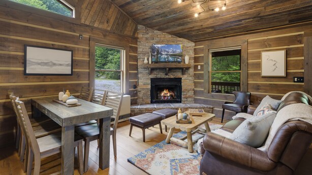 A rustic cabin interior with a stone fireplace, wooden walls, a dining area, and a leather sofa. - Creekside Cabin on Private Acreage (Banner Elk)