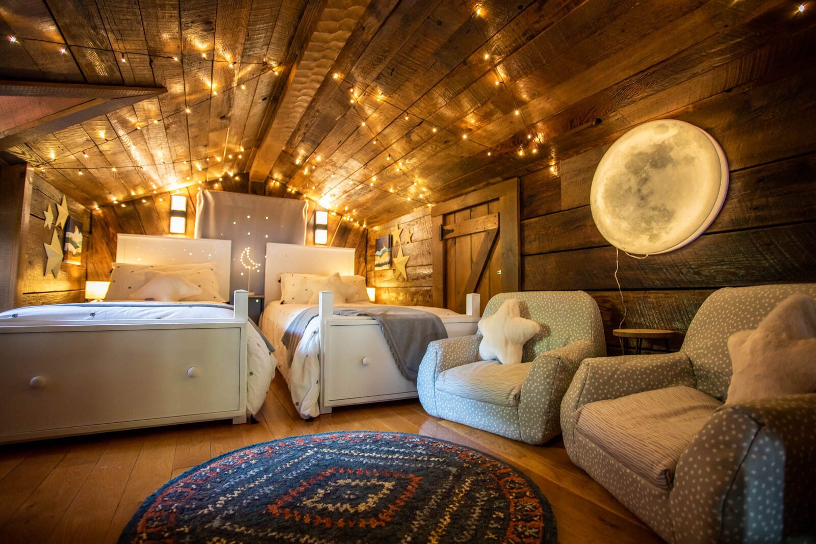 Een knus slaapkamer met twee bedden, een rond vloerkleed en een grote maanversiering aan de muur.