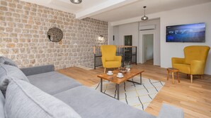 Un salon moderne avec un mur en pierre, un canapé gris, des fauteuils jaunes, une table basse en bois et un téléviseur à écran plat.