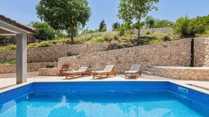 Une piscine avec trois chaises longues en bois et un mur de pierre en arrière-plan.