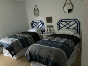 Een slaapkamer met twee bedden, elk met een blauwe hoofdbord, een nachtkastje met een bord waarop staat 'Nee Zeuren' en een spiegel aan de muur.