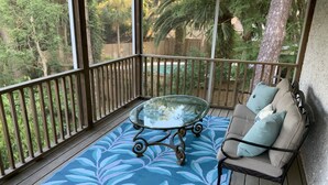 Una veranda coperta con un tavolo dal piano in vetro, un tappeto azzurro con decorazioni e un divano beige con cuscini.