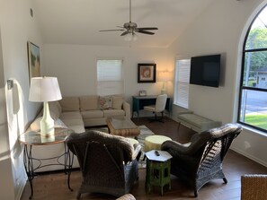 A living room with a sofa, two wicker chairs, a coffee table, a lamp, a TV, and a ceiling fan.
