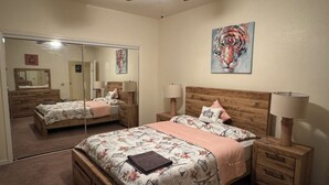 Quarto com cama de madeira, duas mesas de cabeceira com abajures, um espelho grande e um quadro na parede.