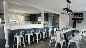 Eine moderne Küche mit Bar, weißen Barhocker und einem Esstisch mit Stühlen.