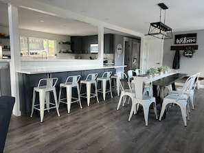 A modern kitchen with a bar area, white bar stools, and a dining table with chairs.