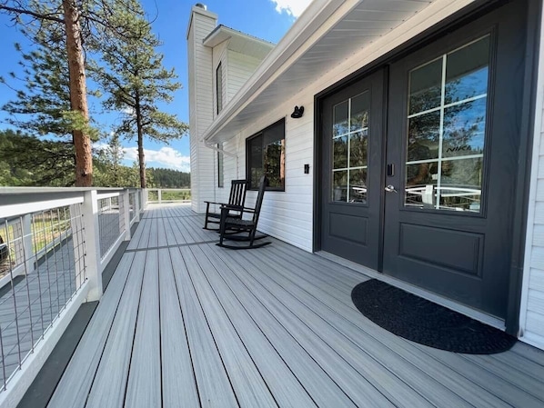 A wooden deck with a rocking chair, a dark door, and a white building with a visible window.