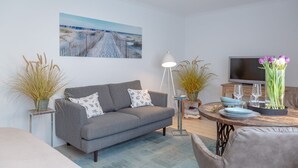 Ein modernes Wohnzimmer mit grauem Sofa, Couchtisch, Fernseher und Zimmerpflanzen.