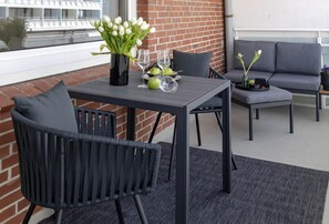 Un espace patio aménagé avec une table, des chaises, un vase de fleurs et un canapé gris.