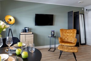 Un salon moderne avec une table à manger ronde, un canapé, un téléviseur fixé au mur et une petite table d’appoint sur laquelle est posé un vase.