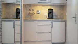 Eine kleine Küche mit weißen Schränken, einer Mikrowelle, einer Kaffeemaschine und einem Spülbecken.