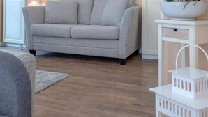 Ein Wohnzimmer mit einem grauen Sofa, einem weißen Beistelltisch mit Schale und Pflanze sowie einer weißen Laterne.