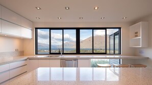 A modern kitchen with a large island, a view of mountains and a lake, and a dining area with a table and chairs.