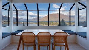 A dining area with a table and chairs, large windows with a mountain view, and a white interior.