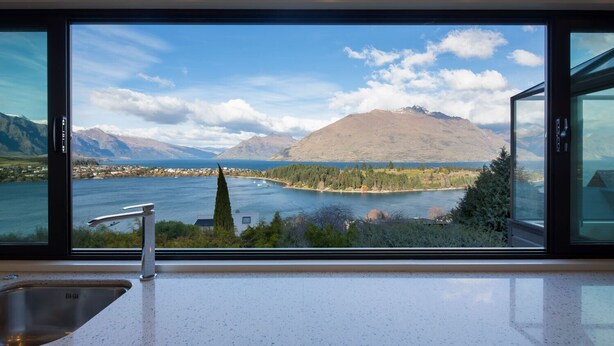 A kitchen with a large window overlooking a lake, mountains, and a small town.