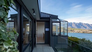 A modern house with a glass balcony overlooking a lake and mountains.
