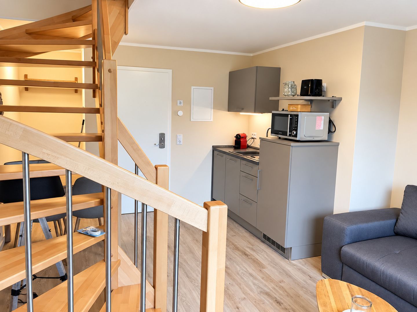 Ein modernes Interieur mit einer Holztreppe, einer Küchenzeile und einem grauen Sofa.