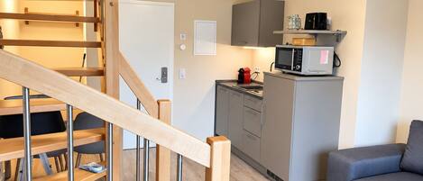 A modern interior with a wooden staircase, a kitchen area, and a grey sofa.