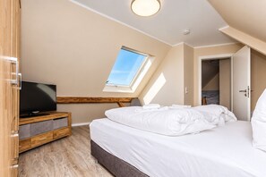 A bedroom with a bed, a television on a wooden stand, a skylight, and a door leading to another room.