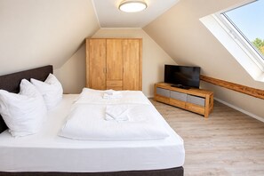 Un dormitorio con cama, almohadas, televisor, armario y ventana.