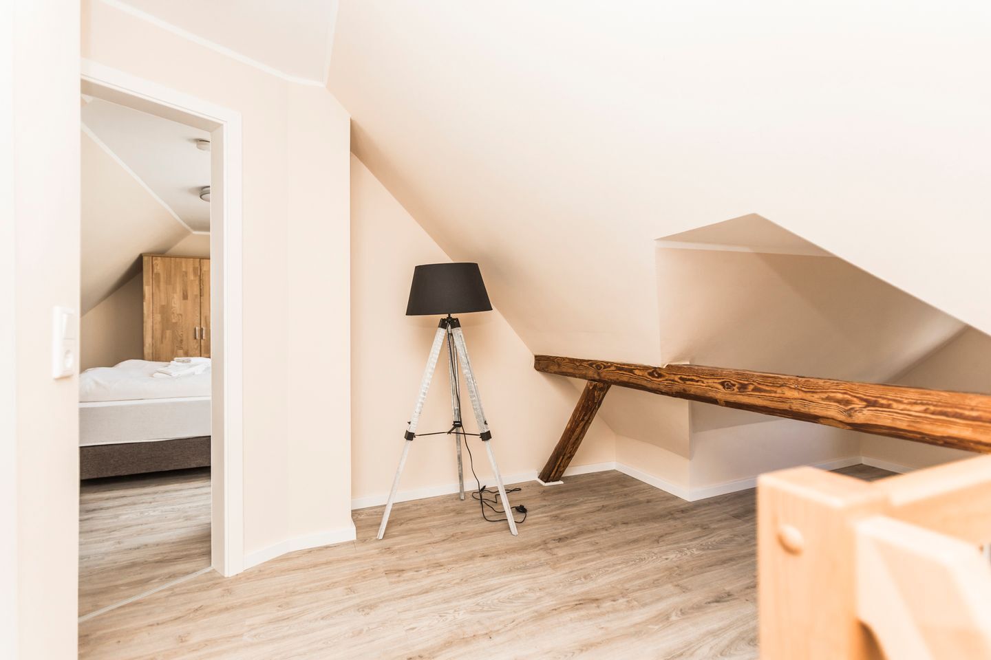 A bedroom with a wooden bed, a tripod lamp, and a wooden beam structure.