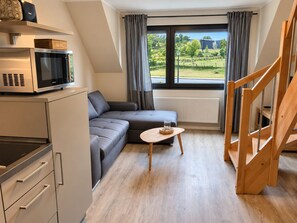 A modern kitchenette with a microwave, a wooden table, and a grey sofa.