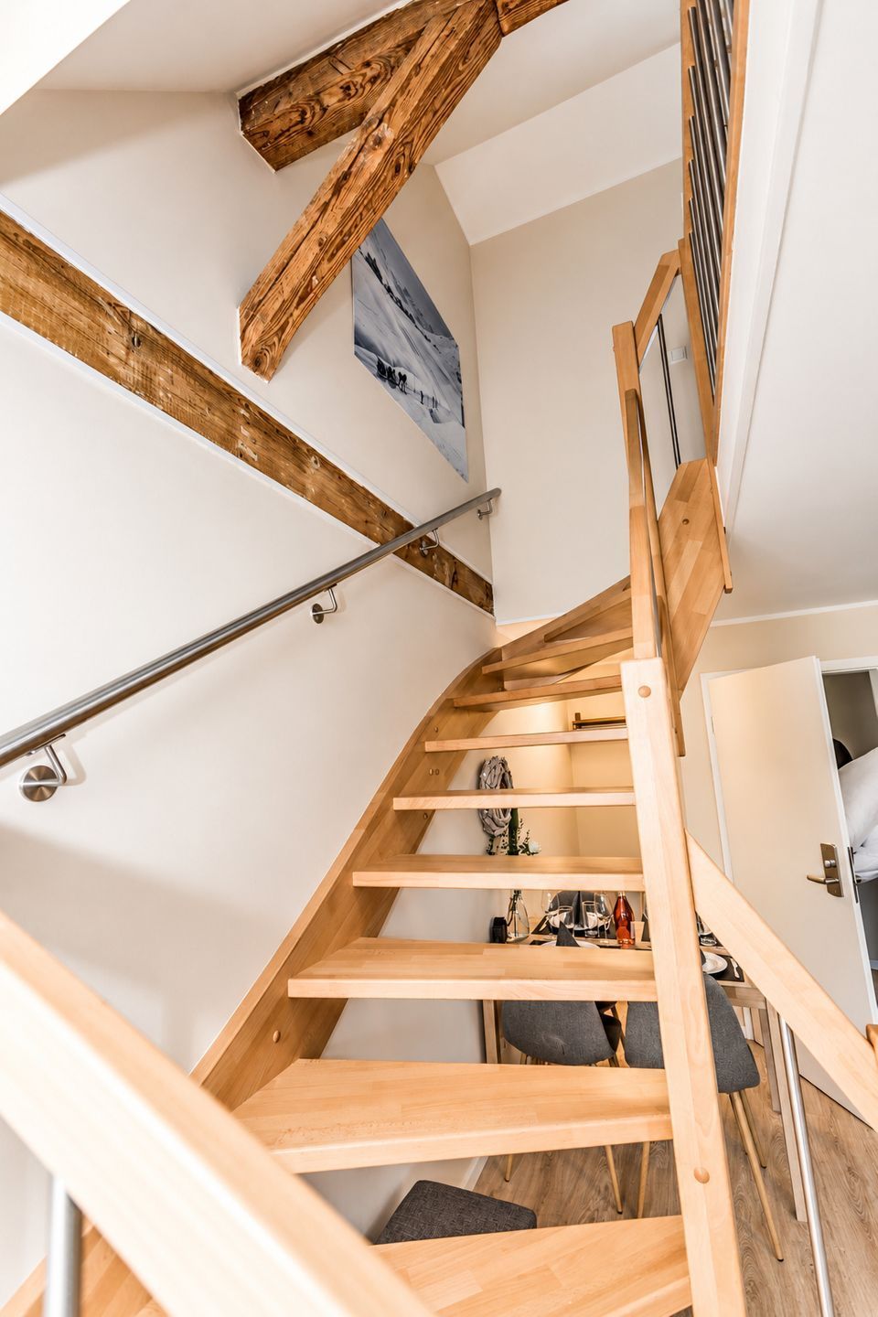 A wooden staircase with a metal handrail, a view of the upper floor, and a door leading to another room.
