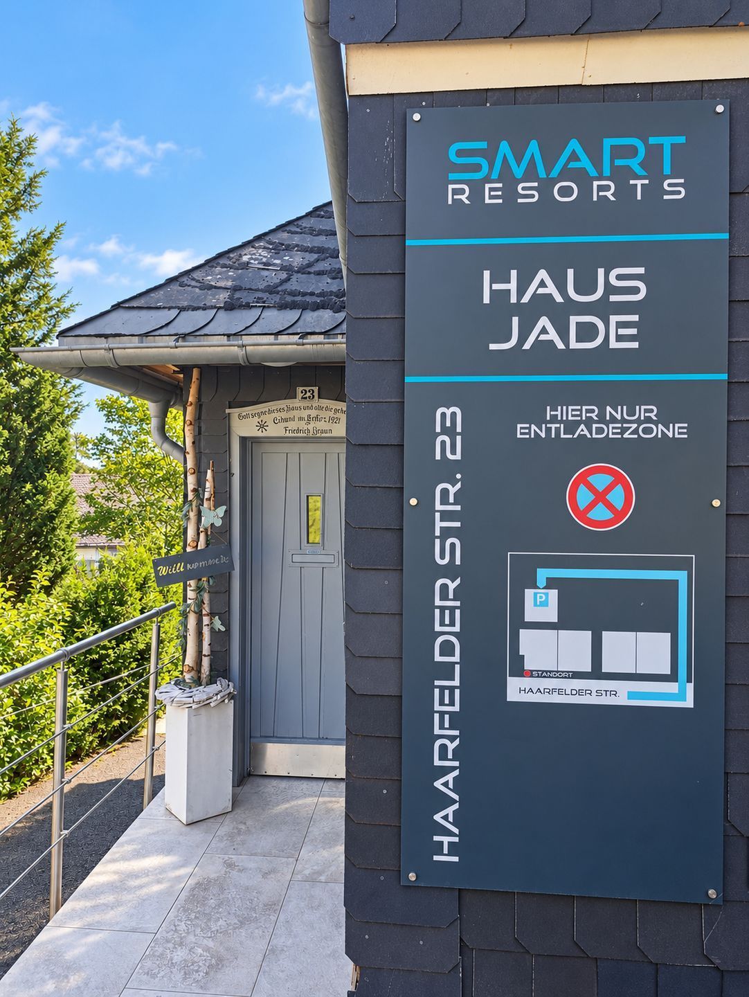 Un panneau indiquant l’emplacement de Smart Resorts HAUS JADE, situé au 23, HAARFELDER STR., et signalant une zone de stationnement avec une zone où le stationnement est interdit.