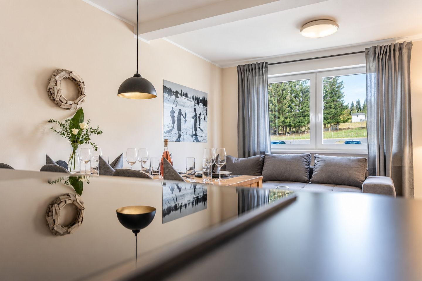 Una sala de estar moderna con comedor, que incluye un sofá, una mesa de centro y una mesa de comedor preparada con vasos y una botella.